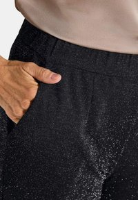 Zwarte broek van een gestructureerde stof met subtiele glans. Voorzien van een zijzak en een elastische tailleband voor een comfortabele pasvorm.