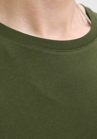 Camiseta de algodón verde oliva con escote redondo, que presenta una textura suave y costuras visibles a lo largo del cuello.