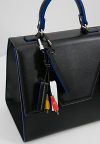 Sac à main en cuir noir et bleu avec un porte-clés comportant des câbles audio-vidéo rouges, jaunes et blancs attachés à la poignée.