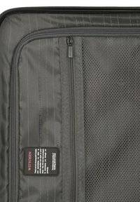 Interior de maleta de tela negra con cremalleras, bolsillo de malla, patrón de rayas verticales y etiqueta de marca. Ideal para organizar objetos.