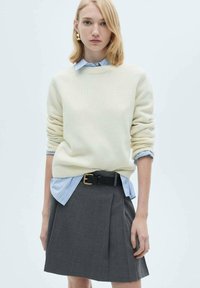 Kremasta pletena sv sweater preko svetlo modre črtaste srajce, v kombinaciji s temno sivo plisirano krilo in črnim pasom z zlatim zaponko.