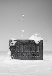 Saponetta nera rettangolare con marchio "STMNT" in rilievo, coperta di schiuma e bolle, su sfondo uniforme.