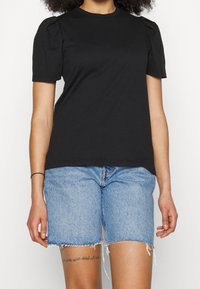 Camiseta de algodón negra con mangas cortas abullonadas, escote redondo y corte holgado, combinada con pantalones cortos de mezclilla azul con dobladillo deshilachado.