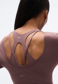 Αθλητικό τοπ Nike σε απαλό μωβ, με σχεδιασμό με λουράκια και ανοίγματα στην πλάτη, και μικρό λογότυπο στη βάση του λαιμού. Λείο υλικό.