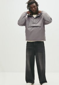 Jachetă pulover gri deschis cu buzunar frontal, glugă ajustabilă și manșete elastice, asortată cu pantaloni din denim negri cu părți late și adidași albi.