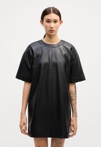 Vestido t-shirt oversized de pele preta, com mangas curtas, decote redondo e detalhes de costura mínimos. Textura suave, comprimento até ao joelho.