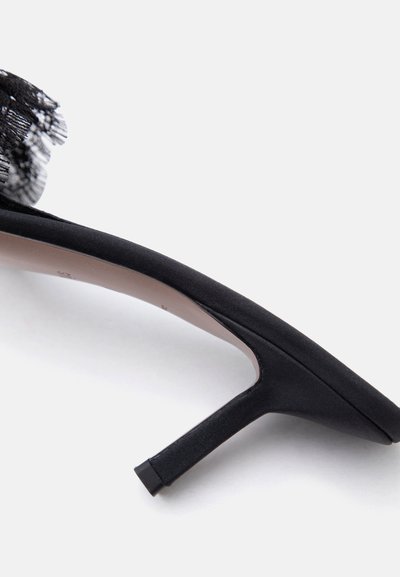 Chaussure à talon haut noire avec pointe pointue, talon fin et détail décoratif en dentelle noire à l'arrière supérieur.