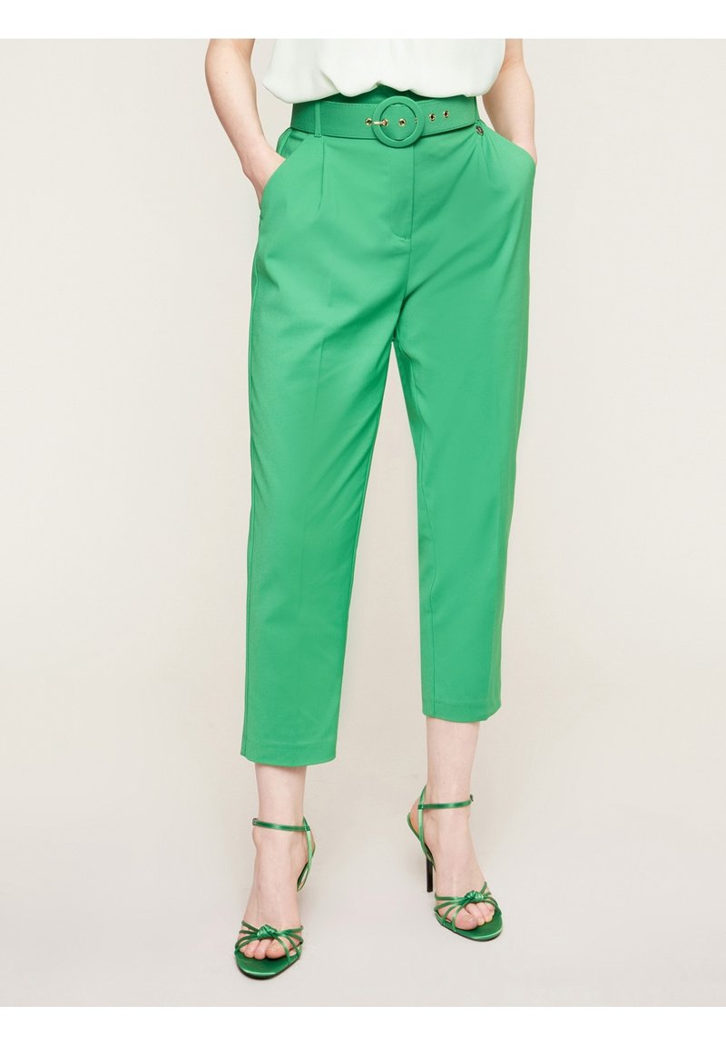 Zelené kalhoty na míru s vysokým pasem, předními kapsami a páskem s kruhovou sponou. Nosit s zelenými sandály na podpatku s pásky. Hladký materiál.