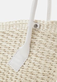 Woven straw tote bag with white leather handle, featuring a smooth texture and a circular metal accent near the handle attachment.