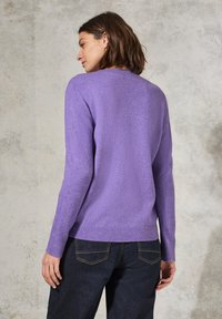 Maglione viola lavorato a maglia con scollo rotondo, polsi e orlo a coste, con una texture morbida. Indossato con jeans scuri.