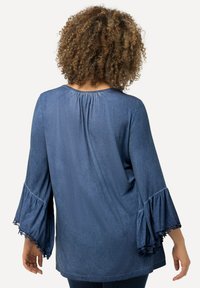 Top in denim con una vestibilità ampia, maniche lunghe a campana con bordi in pizzo, orlo asimmetrico e dettaglio arricciato sul retro del collo.
