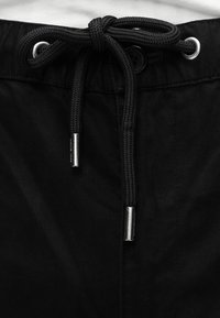 Shorts noirs en tissu texturé, dotés d'un cordon de serrage noir avec embouts argentés et d'une fermeture à bouton à la taille.