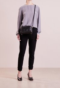 Persona che indossa una blusa lavanda, pantaloni neri attillati, tacchi neri e una borsa a tracolla nera con il logo DKNY sulla parte frontale.