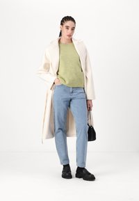 Kremfarget oversized jakke, lys grønn genser, blå jeans, svarte sko, liten svart veske med kjede, glatte teksturer, avslappet passform.