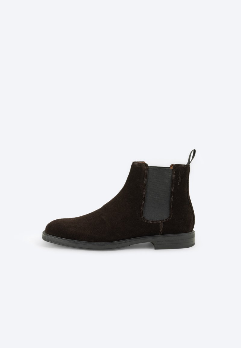 Bottine Chelsea en suede marron avec des panneaux élastiques sur les côtés, une tirette et une semelle en caoutchouc pour une meilleure adhérence. Texture lisse avec un design à bout rond.