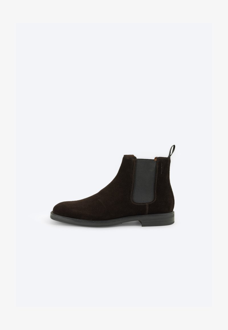 Brown suede Chelsea boot featuring elastic side panels, a pull tab, and a rubber sole for grip. Smooth texture with a rounded toe design.