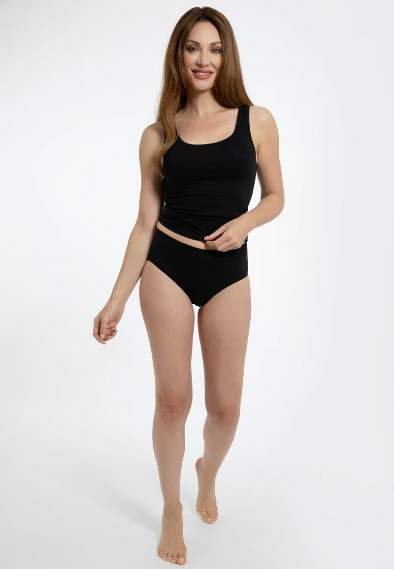 Top in cotone nero a costine e slip bikini a vita alta su una modella, che mettono in evidenza un design aderente e una consistenza morbida su uno sfondo chiaro.