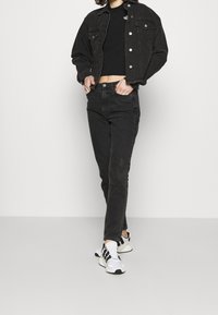 Svart denimjacka med knäppningar, tillsammans med svarta högmidjade jeans. Vita och svarta sneakers fulländar outfiten.