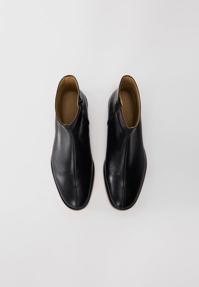 Ein Paar schwarze Lederstiefeletten mit seitlichen Reißverschlüssen, beige Innenfutter, von oben auf einem schlichten weißen Hintergrund gezeigt.