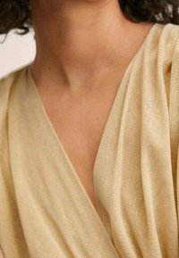 Haut en tissu ivoire doux avec un décolleté en V profond et des manches plissées, mettant en valeur une surface lisse et texturée.