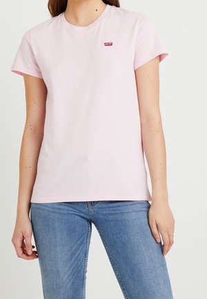 T-shirt en coton rose avec des manches courtes et un col rond. Présente un petit logo rouge de Levi's sur la poitrine. Associé à un jean bleu.