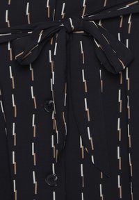 Tissu noir avec des lignes verticales blanches et beiges. Comprend une ceinture nouée, des boutons et un motif texturé.