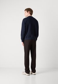 Marineblå hettegenser med ribbestrikkede ermer og hem, kombinert med svarte bukser med avslappet passform. Hvite joggesko fullfører det uformelle utseendet.