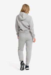 Grå sweatshirt och joggers-set, tillverkat av mjukt tyg, med huva, elastiska muddar och midja, parat med svarta träningsskor.
