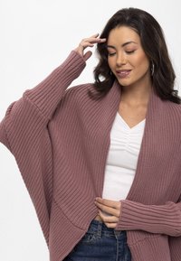 Strickjacke in staubigem Rosé, mit einem groben Rippmuster, offener Vorderseite, weiten Ärmeln und einer fließenden Silhouette.