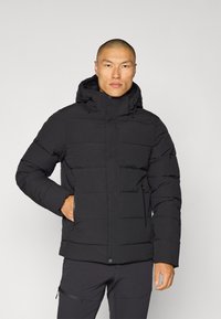 Giacca a vento nera con cappuccio, dotata di chiusura lampo frontale, design trapuntato e due tasche laterali. Texture liscia e dettagli minimali.