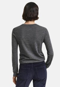 Maglione grigio a maniche lunghe con scollo rotondo, realizzato in un tessuto morbido, caratterizzato da una forma aderente e una consistenza liscia, indossato con pantaloni di velluto a coste blu.