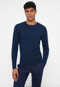 Suéter tricotado azul marinho com mangas longas e decote redondo. O tecido é liso com uma textura subtil, em forma ajustada.
