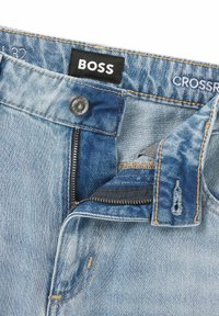 Blå denimjeans med en BOSS-etikett. Har dragkedja och knappstängning, kontrasterande sömmar och en lätt blekning i tyget.