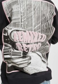 Black sweatshirt featuring a prominent retro car graphic in grayscale, bordered by a pink outline, and "REMIXED RETRO" in raised pink letters.