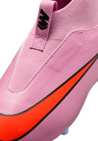 Różowy but piłkarski z dużym czerwono-czarnym logo Nike, teksturowaną powierzchnią i czarnym logo na różowej pętelce z tyłu kołnierza.