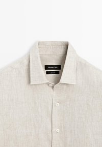 Light beige linen shirt with a classic collar, single pocket, and button front. Textured fabric features a subtle weave pattern.