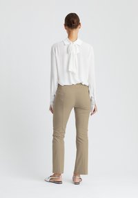 White blouse with collar and bow tie at the back, paired with beige fitted trousers. Silver slip-on shoes with textured detailing.