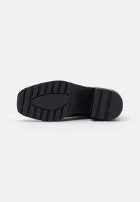 Suela de zapato negra con un material de goma texturizado y profundas ranuras para tracción. Forma plana y rectangular con un acabado suave.