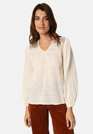 Blouse de couleur crème en tissu léger, dotée d'un col en V, de détails brodés et de longues manches bouffantes avec des accents en dentelle.