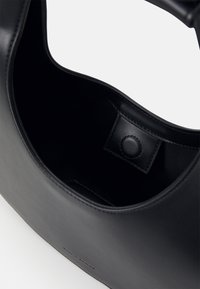 Sac à main en cuir noir avec un bord supérieur courbé et une fermeture à bouton-pression visible à l'intérieur du sac.