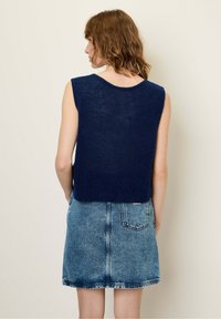 Granatowy, dzianinowy top bez rękawów z okrągłym dekoltem, w zestawie z jasnoniebieską spódnicą dżinsową z tylnymi kieszeniami i wyblakłym wykończeniem.