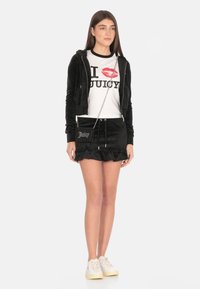 Felpa nera in velluto con zip abbinata a una gonna mini con ruches, T-shirt bianca con labbra rosse e testo nero, abbinata a sneakers bianche.