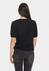 Svart kortärmad stickad topp med rund halsringning, med en kroppsnära passform och ribbad nederkant, ihop med mörkgrå tajta jeans.