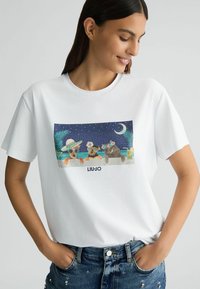 Balti medvilninė marškinėlių su spalvinga grafika, vaizduojančia tris gyvūnus po naktiniu dangumi, su dekoratyviniais akcentais ir "LIU JO" logotipu.