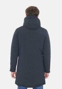 Parka blu scuro con cappuccio, caratterizzata da un taglio lungo, texture liscia e dettagli di cucitura minimi, progettata per garantire calore e copertura.