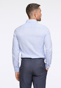 Lichtblauwe lange mouw shirt met een klassieke kraag, gladde textuur en knoopmanchetten, gecombineerd met donkere broeken met achterzakken.