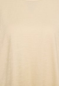 Beige kortärmad topp gjord av ett mjukt, lätt tyg med en slät textur och subtil lyster; har en rundad halsringning och en avslappnad passform.