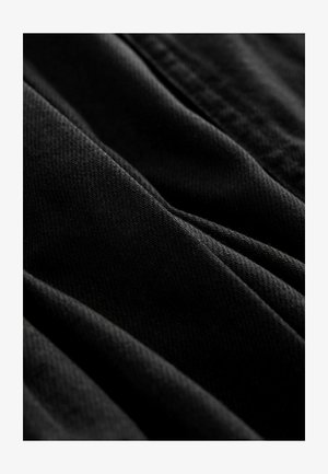 Schwarzer Stoff mit einer strukturierten diagonalen Webart, der sanfte Falten und glatte Kanten aufweist und auf ein leichtes sowie flexibles Material hinweist.