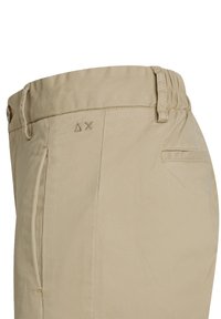 Pantaloni di cotone beige con una texture liscia, dotati di chiusura a bottone, tasche laterali e delicate rifiniture ricamate in vita.