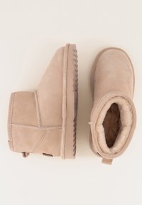 Beige suède enkellaarsjes met een gestructureerde rubberen zool, schapenvachtvoering en een trekband bij de hiel. Glad exterieur met stiknaaddetails.